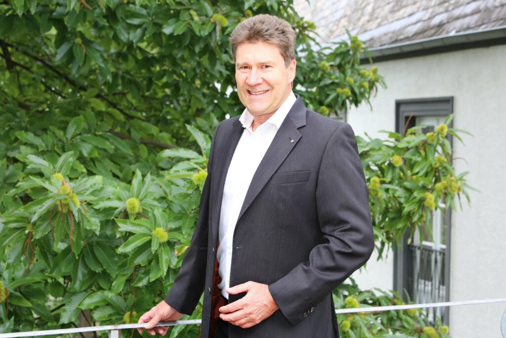 Der Unternehmensberater und Gründer von consultingcheck, Dr. Werner Boysen, posiert an einem Geländer vor einem Baum.